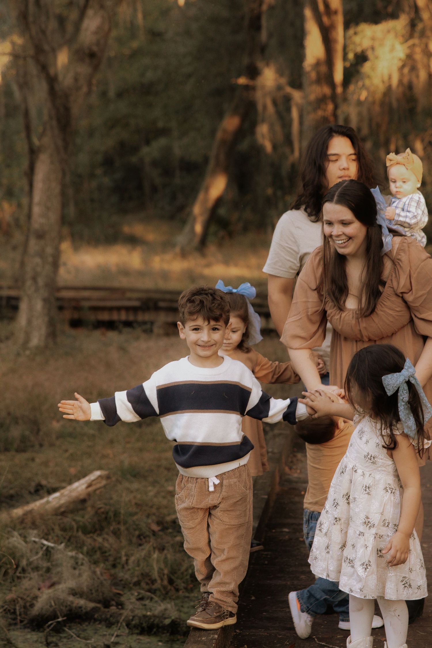 A young child spreads their arms wide with joy while others watch in a wooded setting.