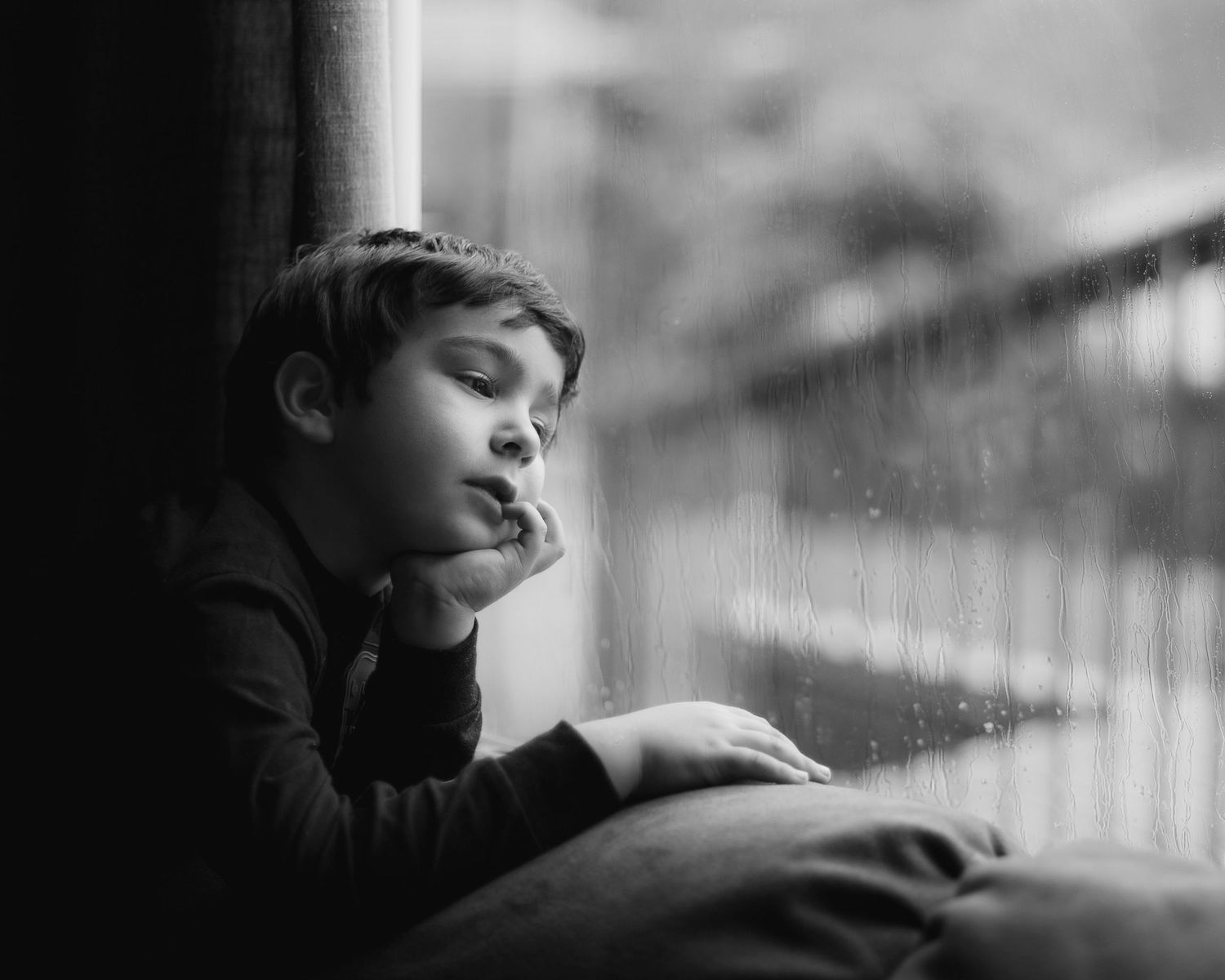 A dreamy black and white photograph of a child gazing out of a window pensively.