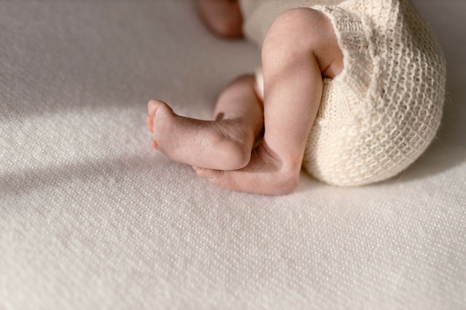 Tiny baby foot wrapped in a cozy white knit blanket rests on soft beige fabric.