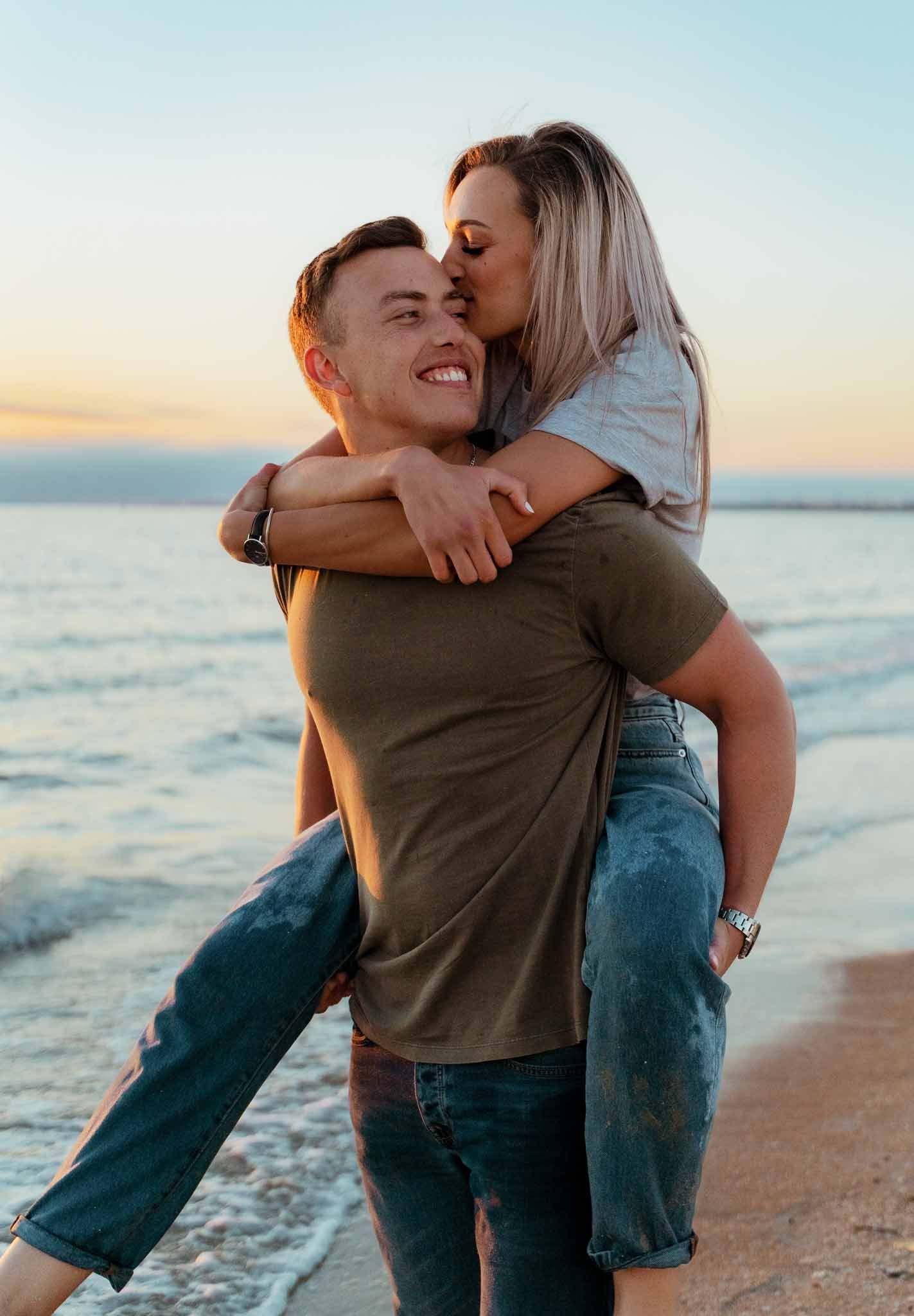 Couple sharing playful piggyback ride moment on beach at sunset.