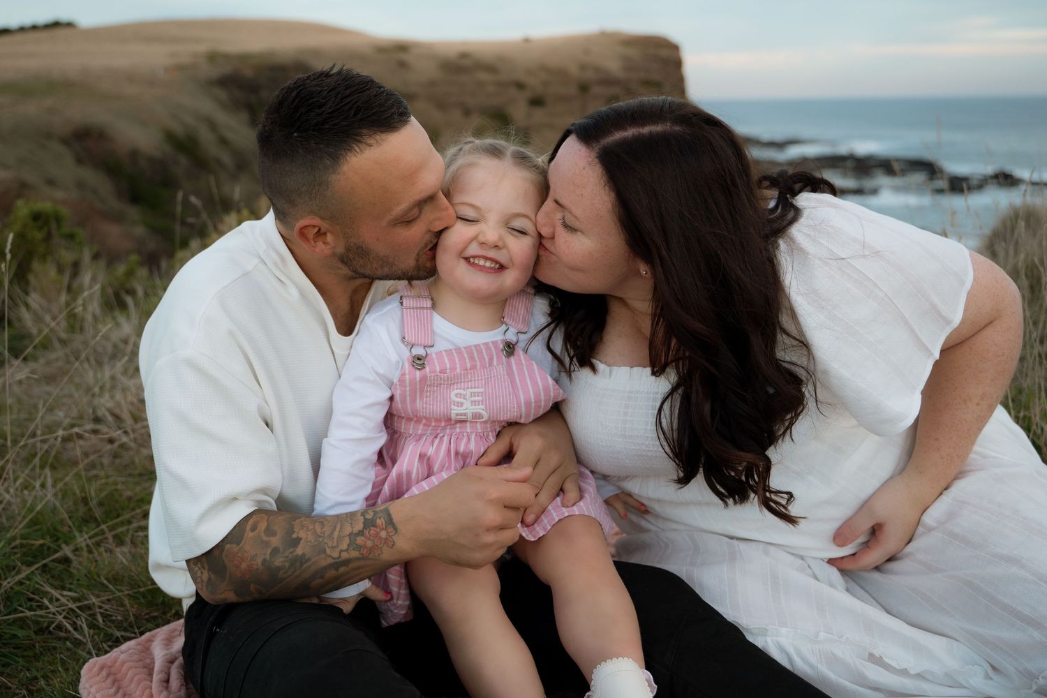 A happy family shares a tender moment together on a coastal hillside during golden hour.