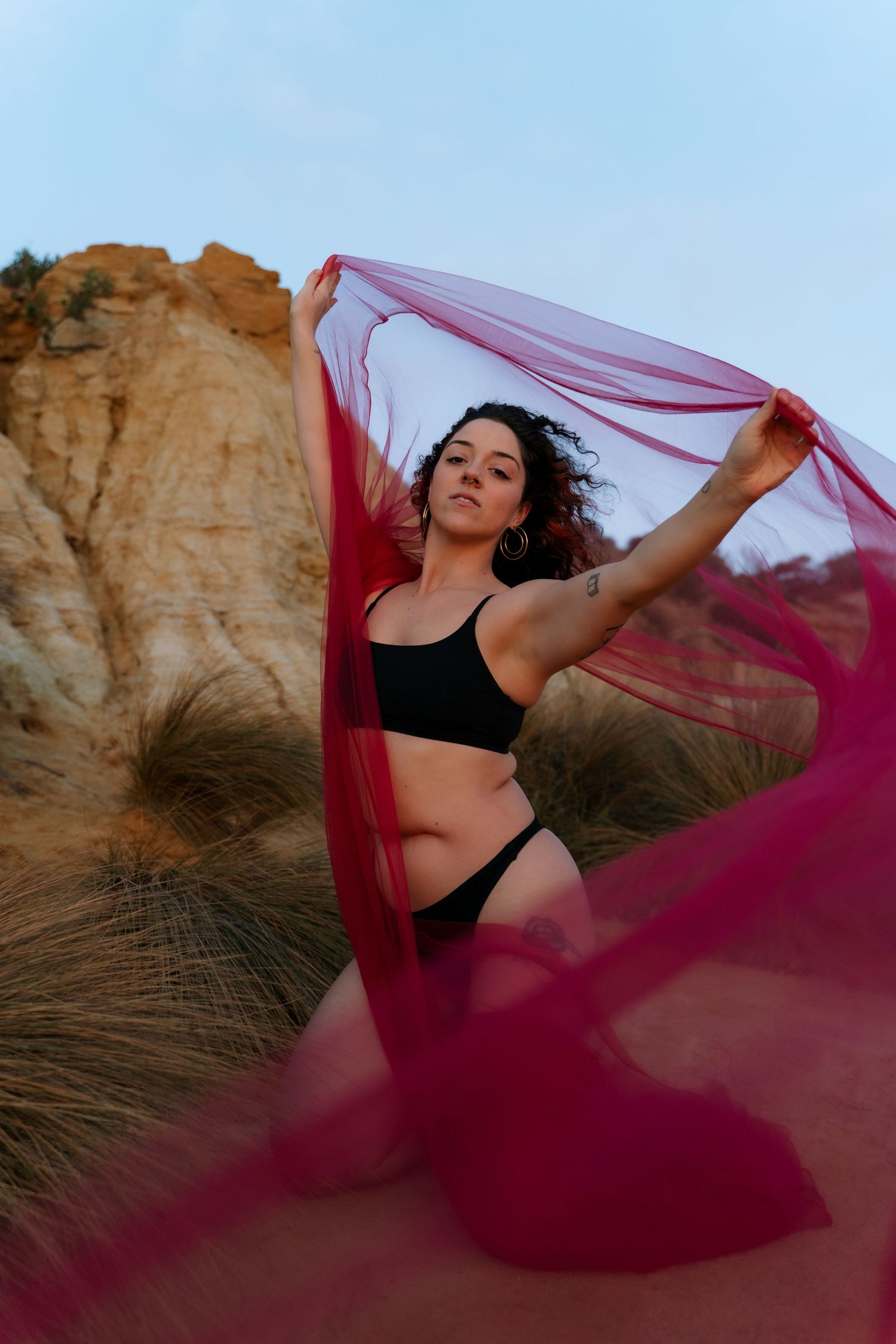 A dancer in black athletic wear moves gracefully with flowing red fabric against desert rock formations at sunset.