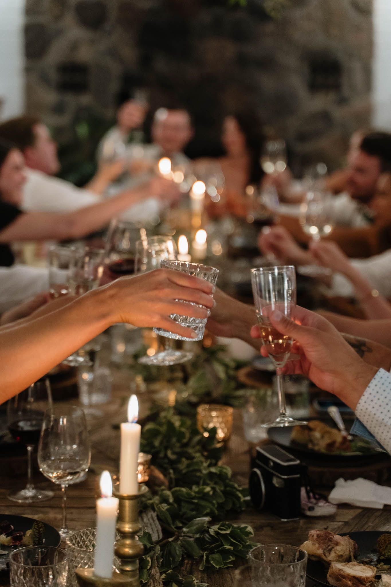 Candlelit wedding reception table with guests toasting glasses.