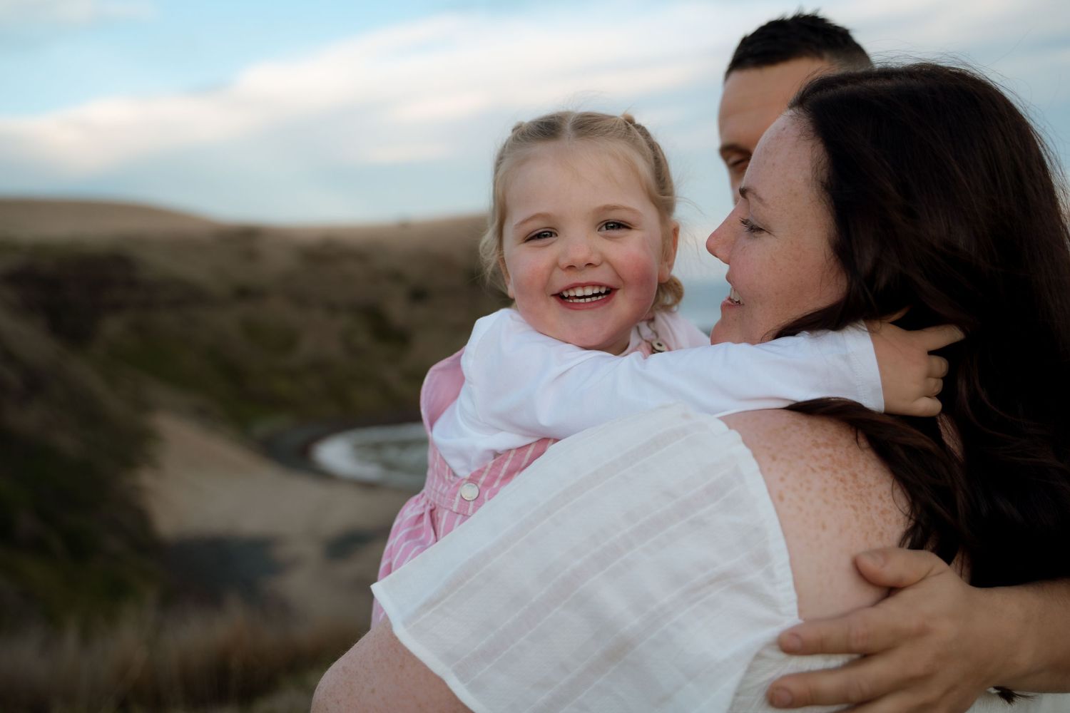 A parent and child share a heartwarming embrace outdoors against a scenic natural landscape during golden hour.