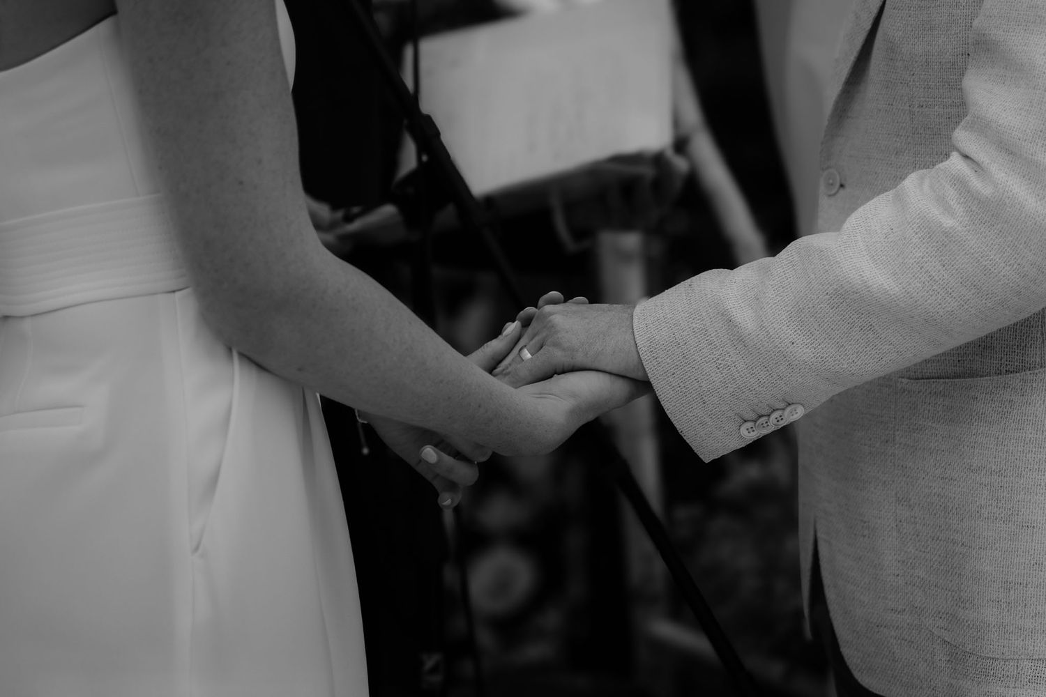 Black and white close-up of hands exchanging rings during wedding ceremony.