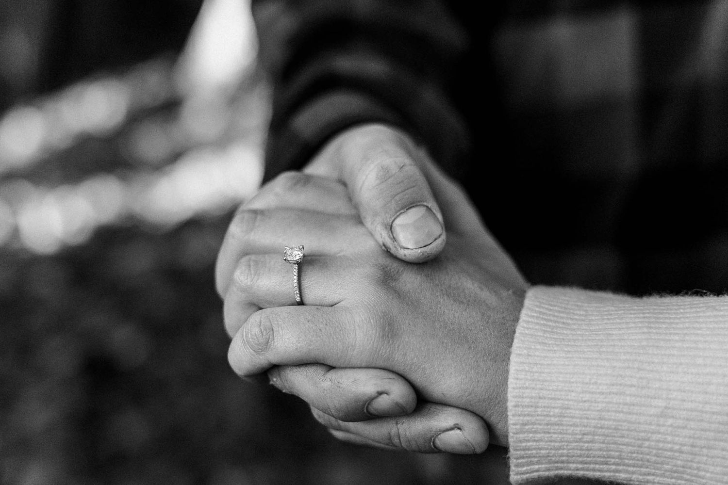Close up of intertwined hands with engagement ring in black and white.