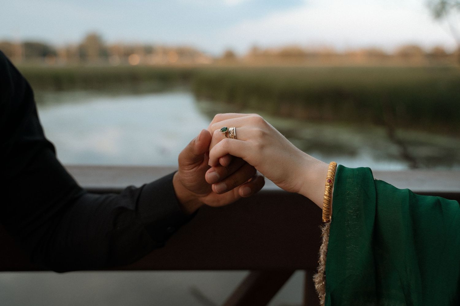 Hands exchanging a gold ring during a romantic lakeside proposal at sunset.