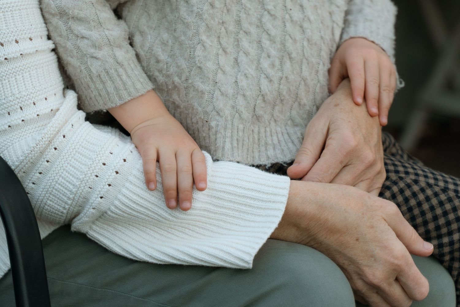 Close-up of three generations of hands resting together, showing a child, adult, and elderly person in a touching family moment.