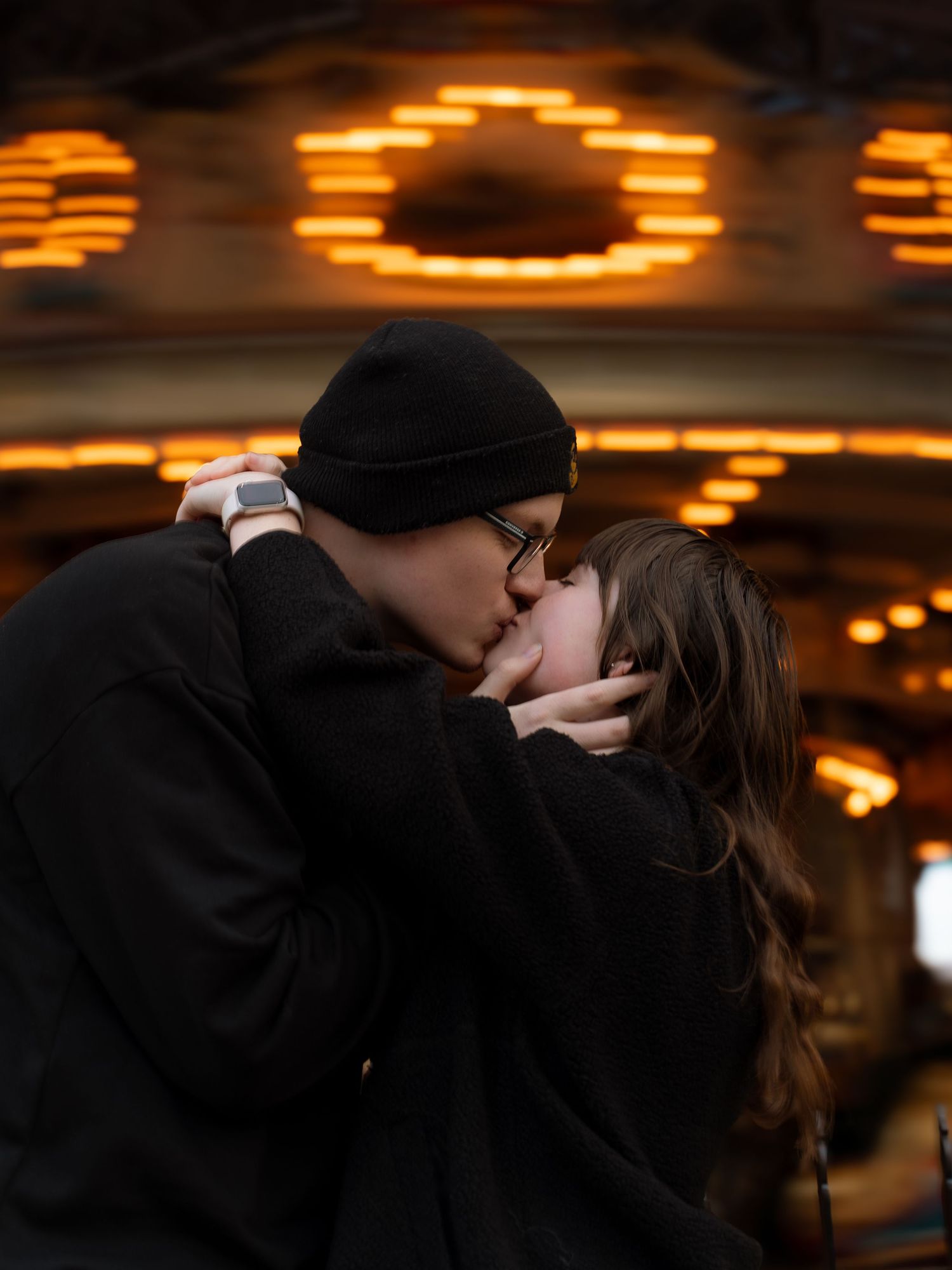 A romantic couple shares an intimate kiss under illuminated circular lights at dusk creating a warm ambiance.