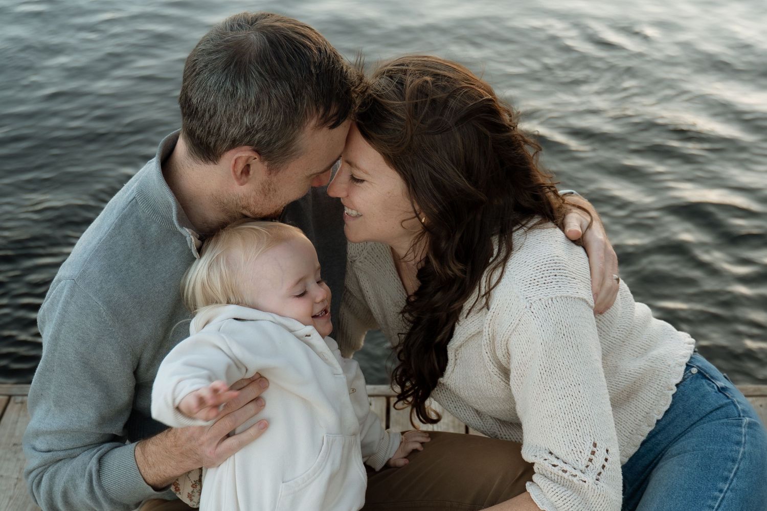A couple shares a tender moment kissing over their sleeping baby by a serene lake.