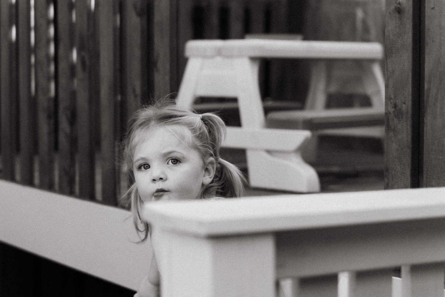 A black and white photo of a small child peeking over the edge of a railing with wide-eyed curiosity.