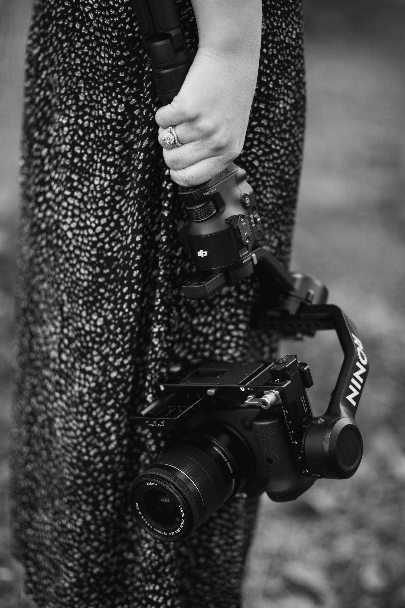 Black and white image of a hand holding a Nikon DSLR camera against a patterned fabric background.