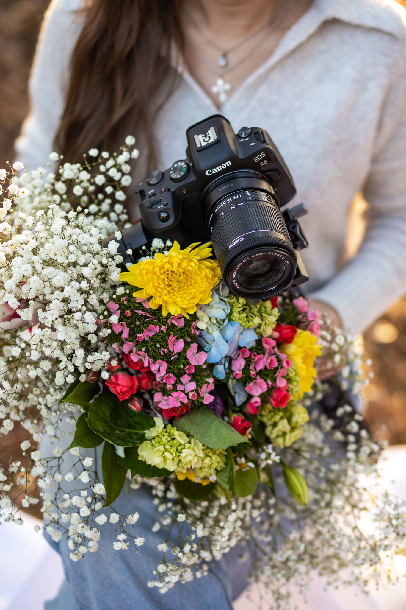 Canon DSLR camera nestled in a colorful bouquet with yellow daisies, baby's breath, and pink flowers.