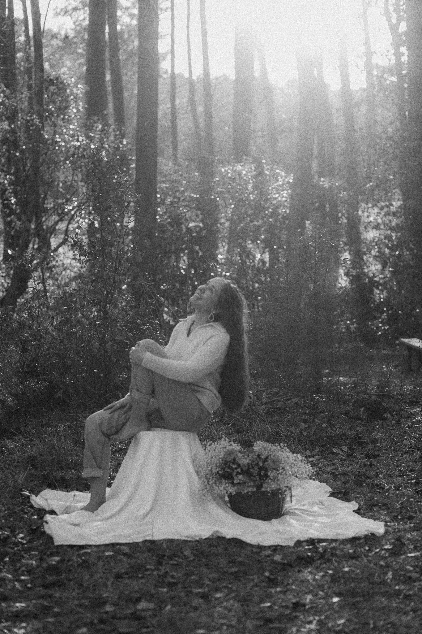 A dreamy black and white photograph shows a figure sitting on a blanket in a misty forest setting.