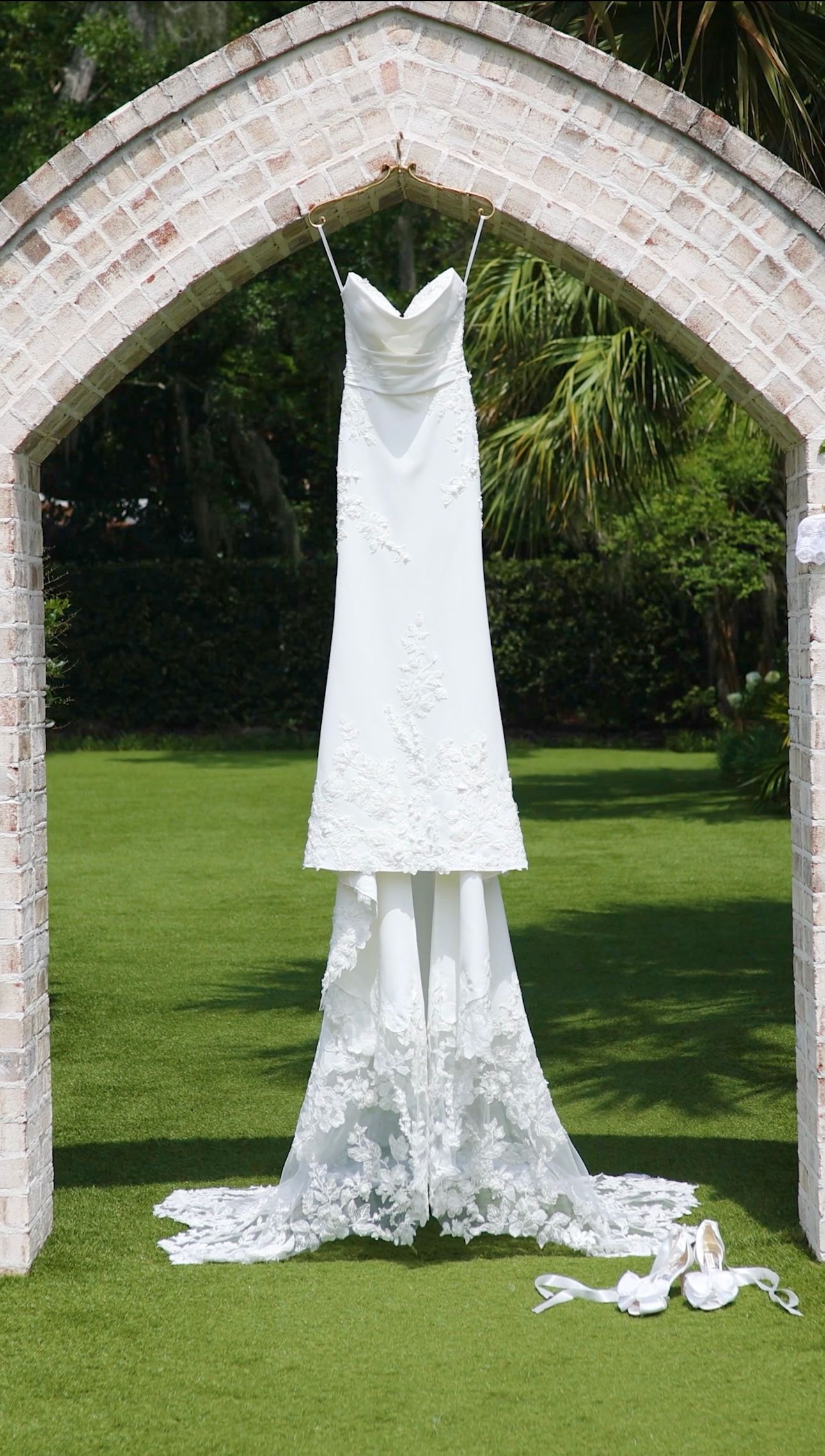 White wedding dresses displayed on archways in a lush garden setting with green grass and natural lighting.