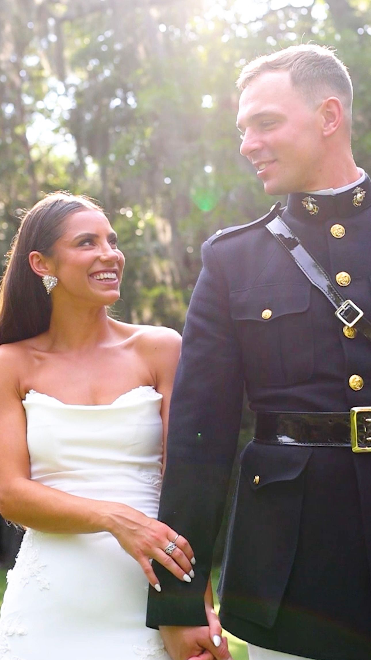Happy couple shares a joyful moment during their wedding as the bride in white and military groom embrace outdoors.