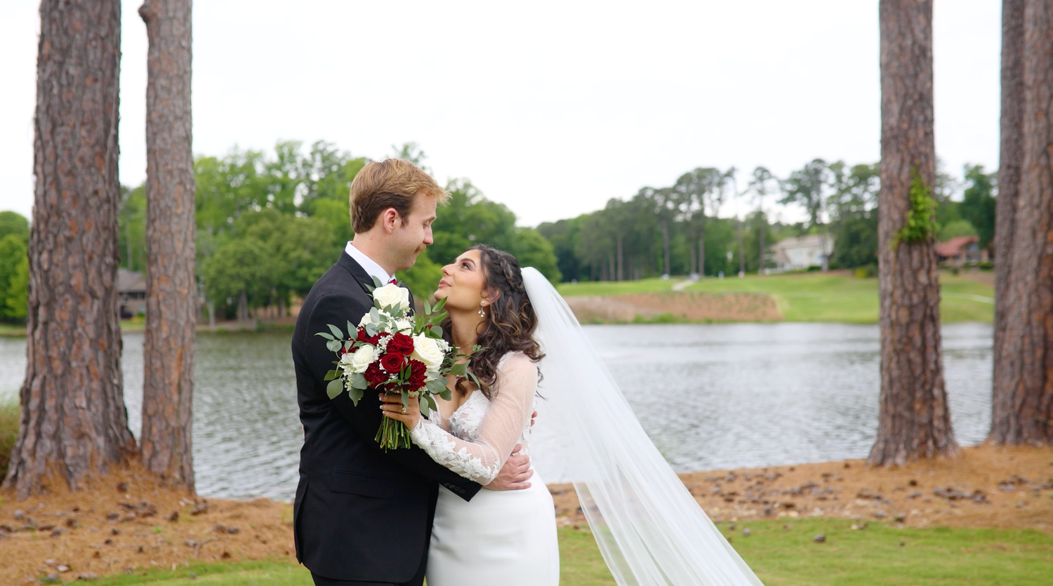 Joyful wedding couple shares intimate embrace near lake surrounded by towering pine trees at sunset.