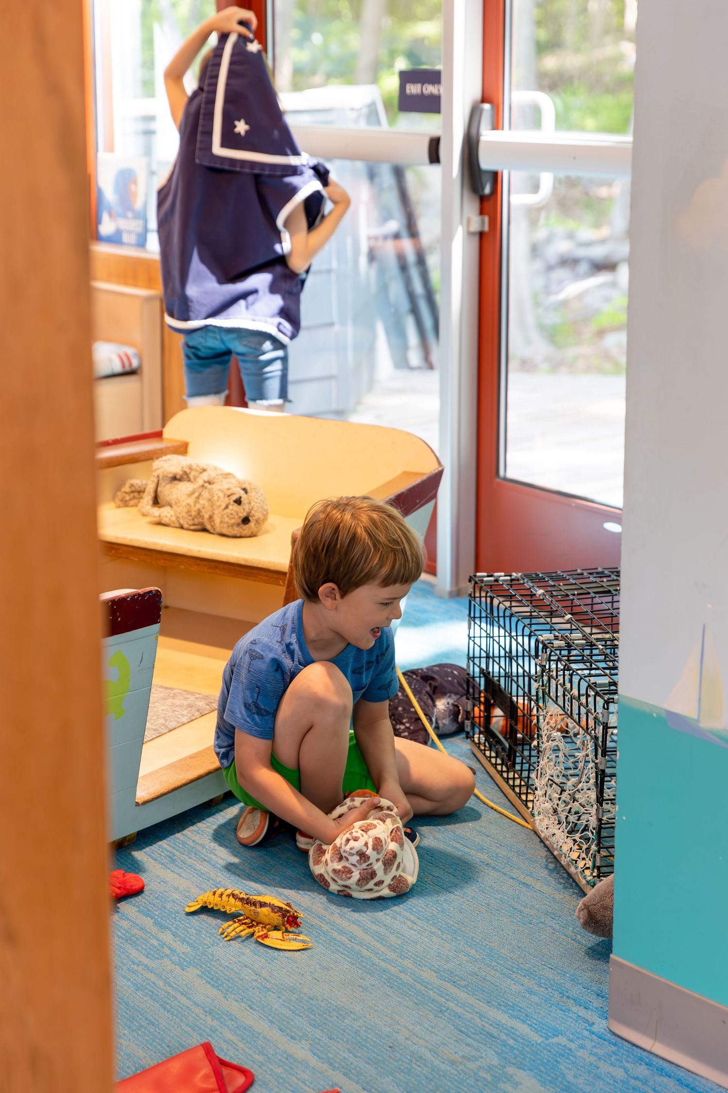 Four children kneel on a blue floor examining small animals in cages at what appears to be a pet store.