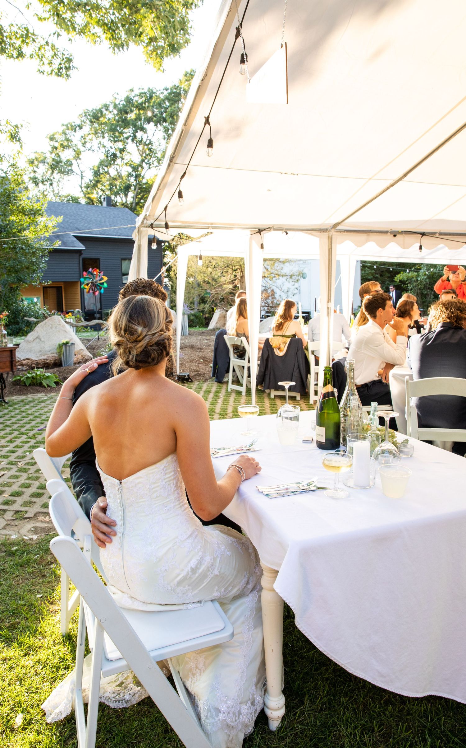 Intimate outdoor wedding reception under white tent canopy with round tables decorated in crisp white linens and floral centerpieces.