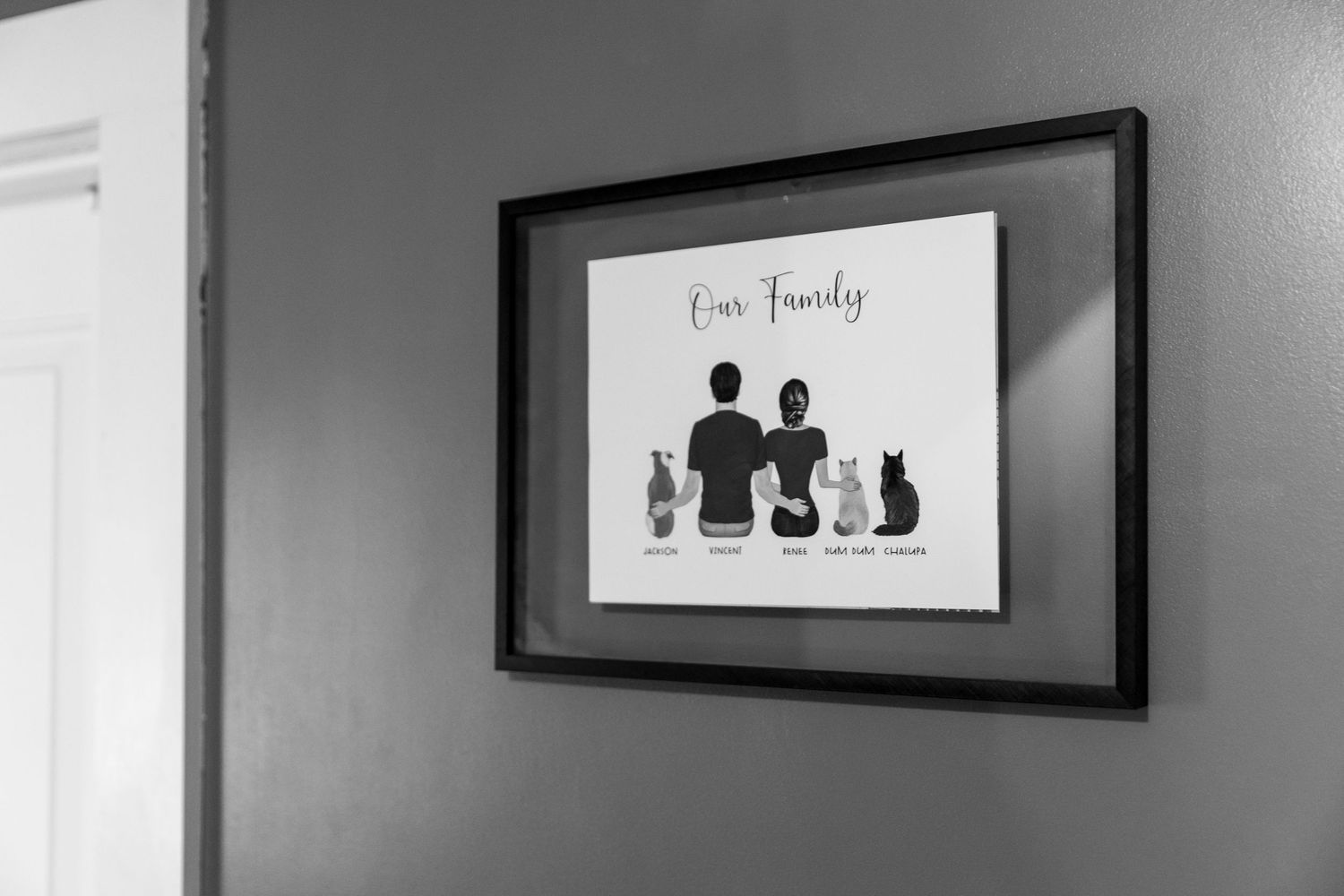 A black and white framed artwork showing silhouettes of people and cats with text 'Our Family' hangs on a white wall.