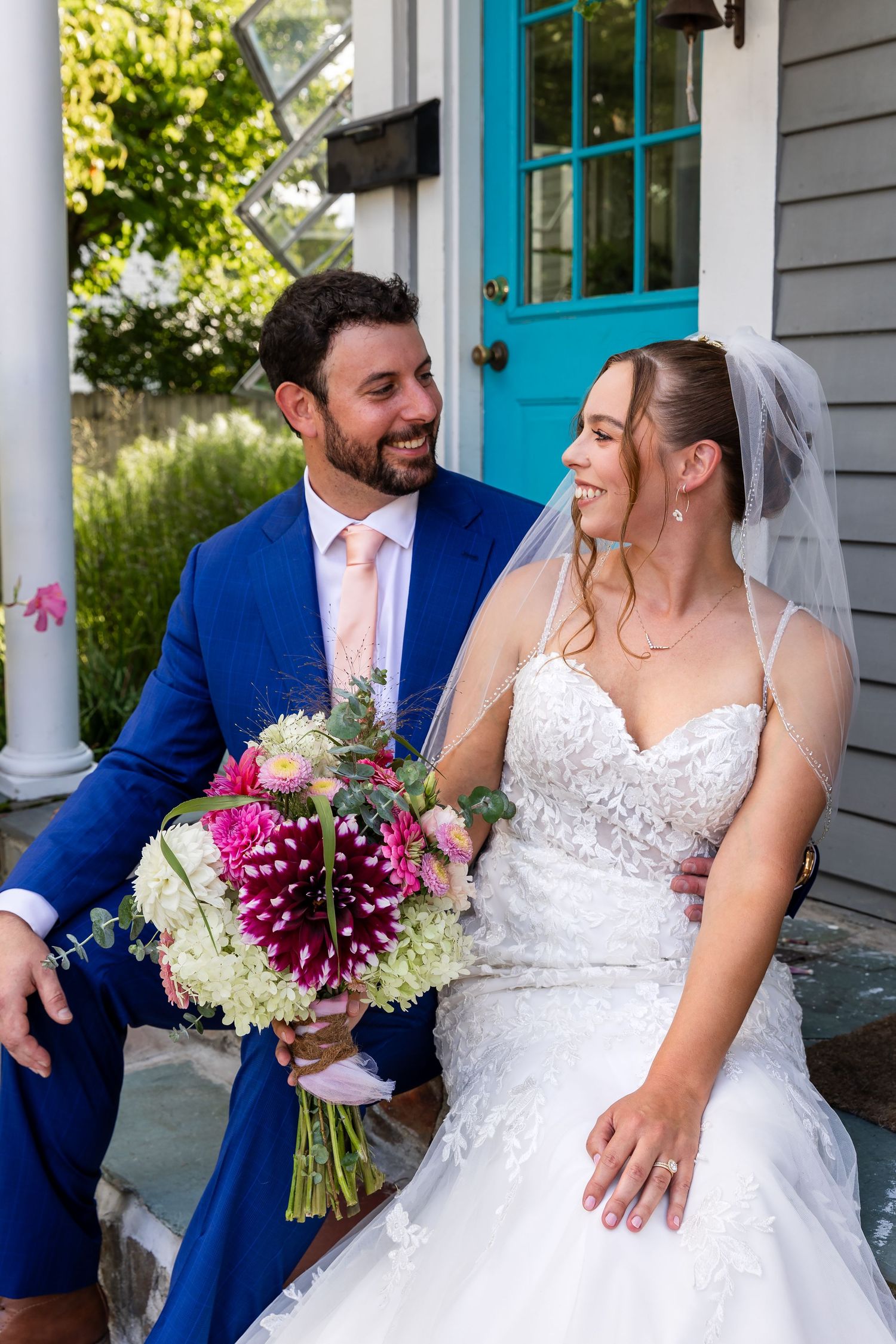 A joyful wedding couple shares loving moments on a porch with white columns and blue trim during their celebration.