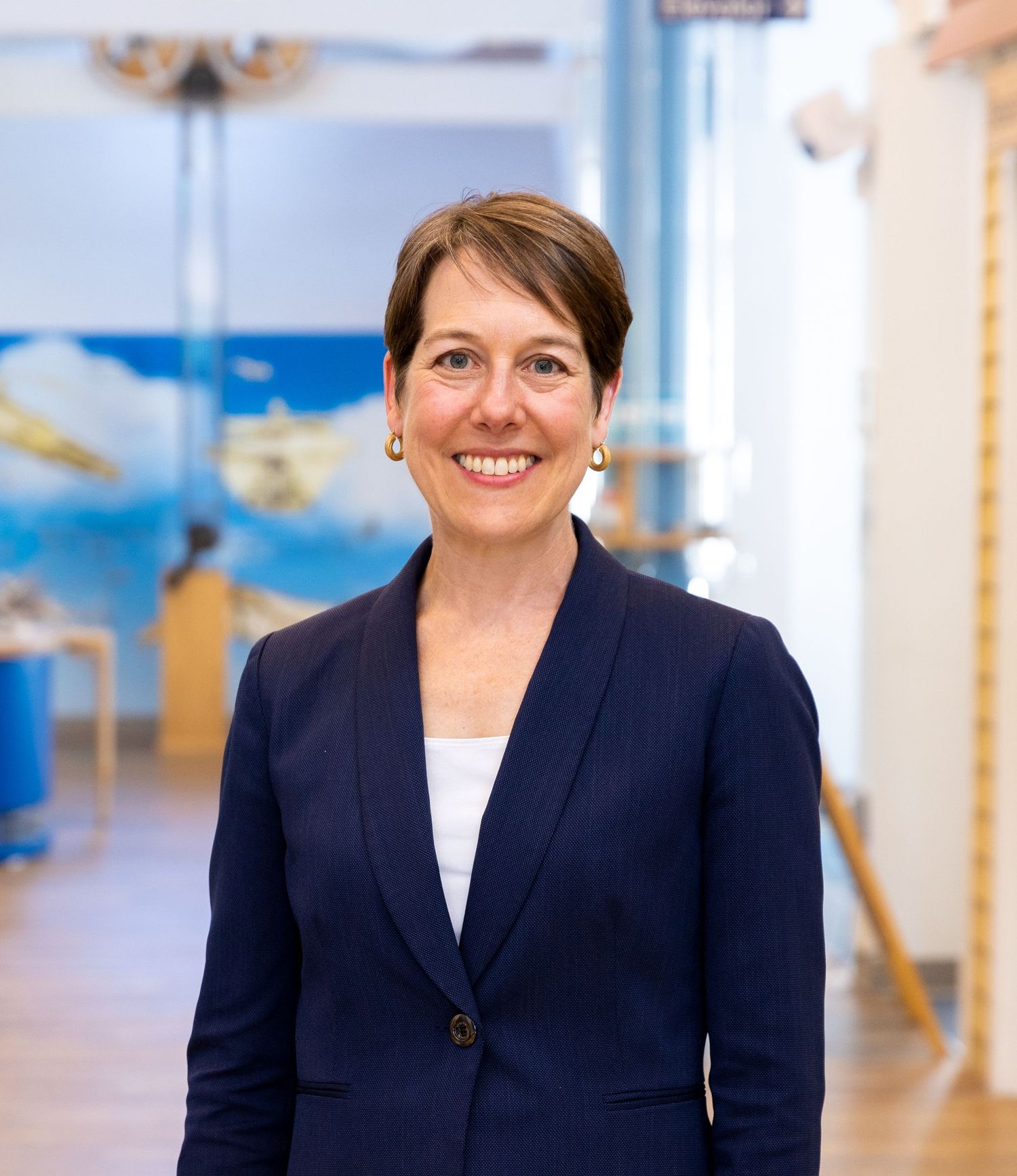 A woman wearing a navy blazer and white shirt smiles professionally in an office setting.