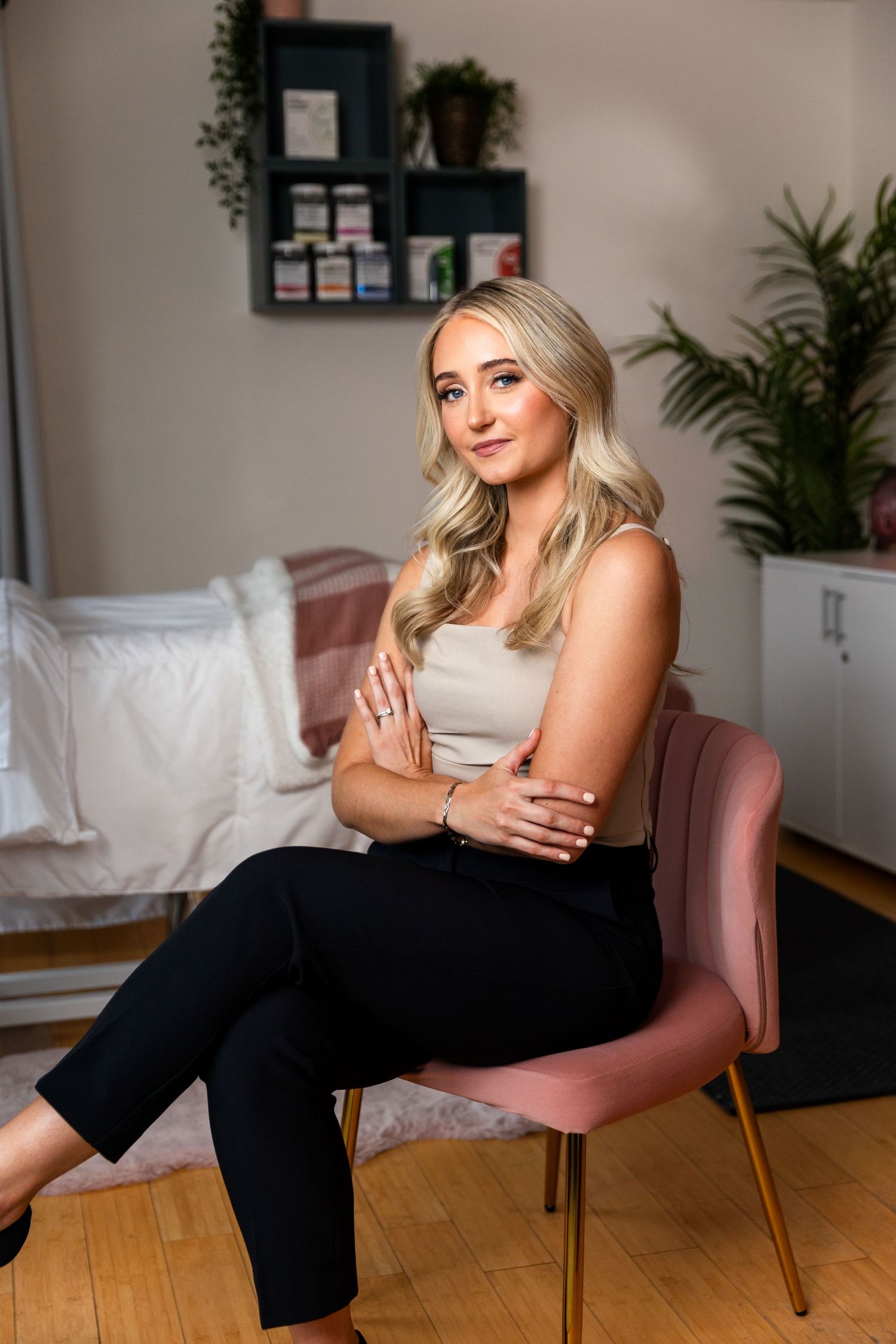 A person sits relaxed in a pink velvet chair wearing a casual gray tank top and black pants in a modern living room setting.