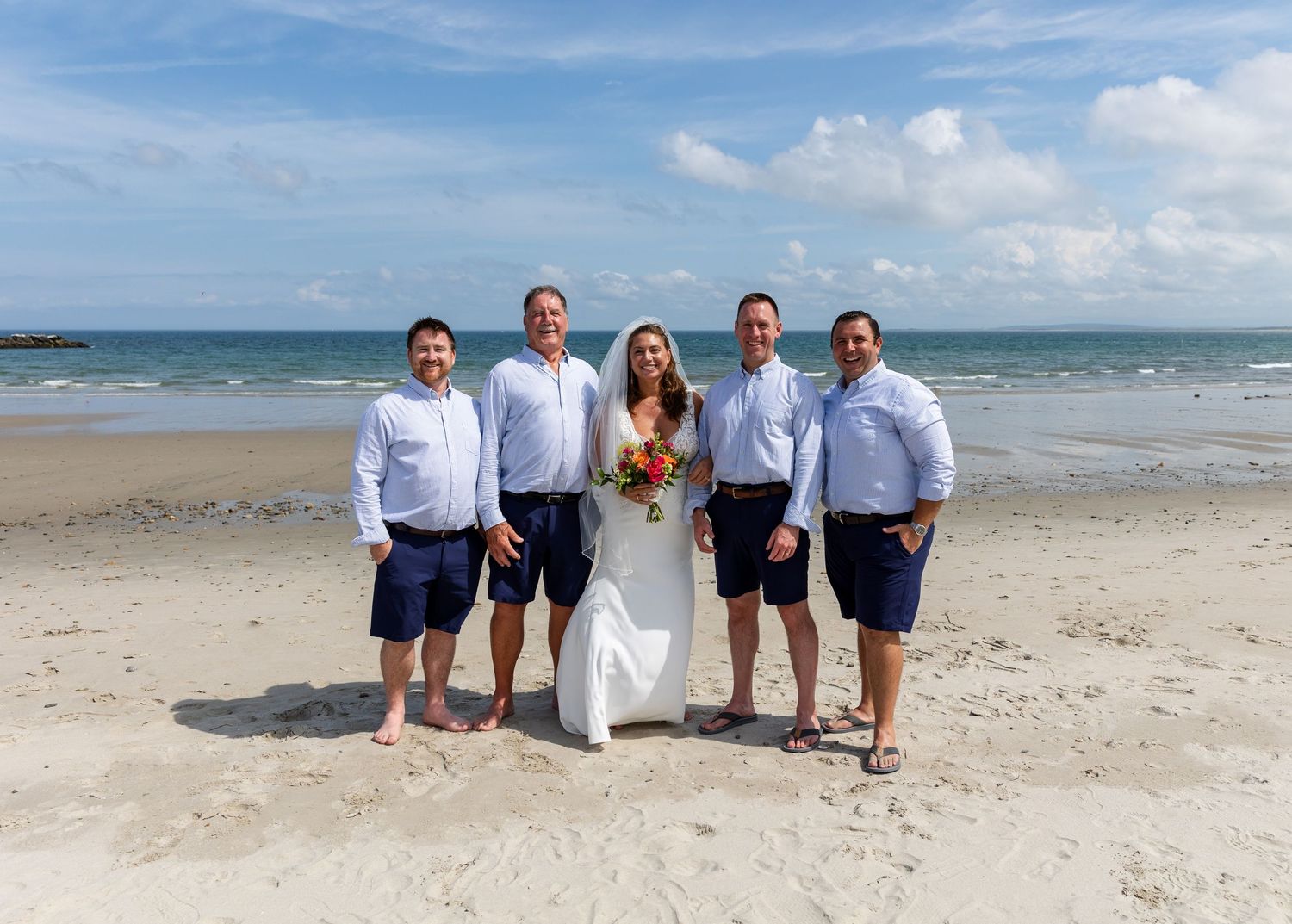 Group of beachgoers sitting casually together on white sand with ocean waves and blue sky in the background.