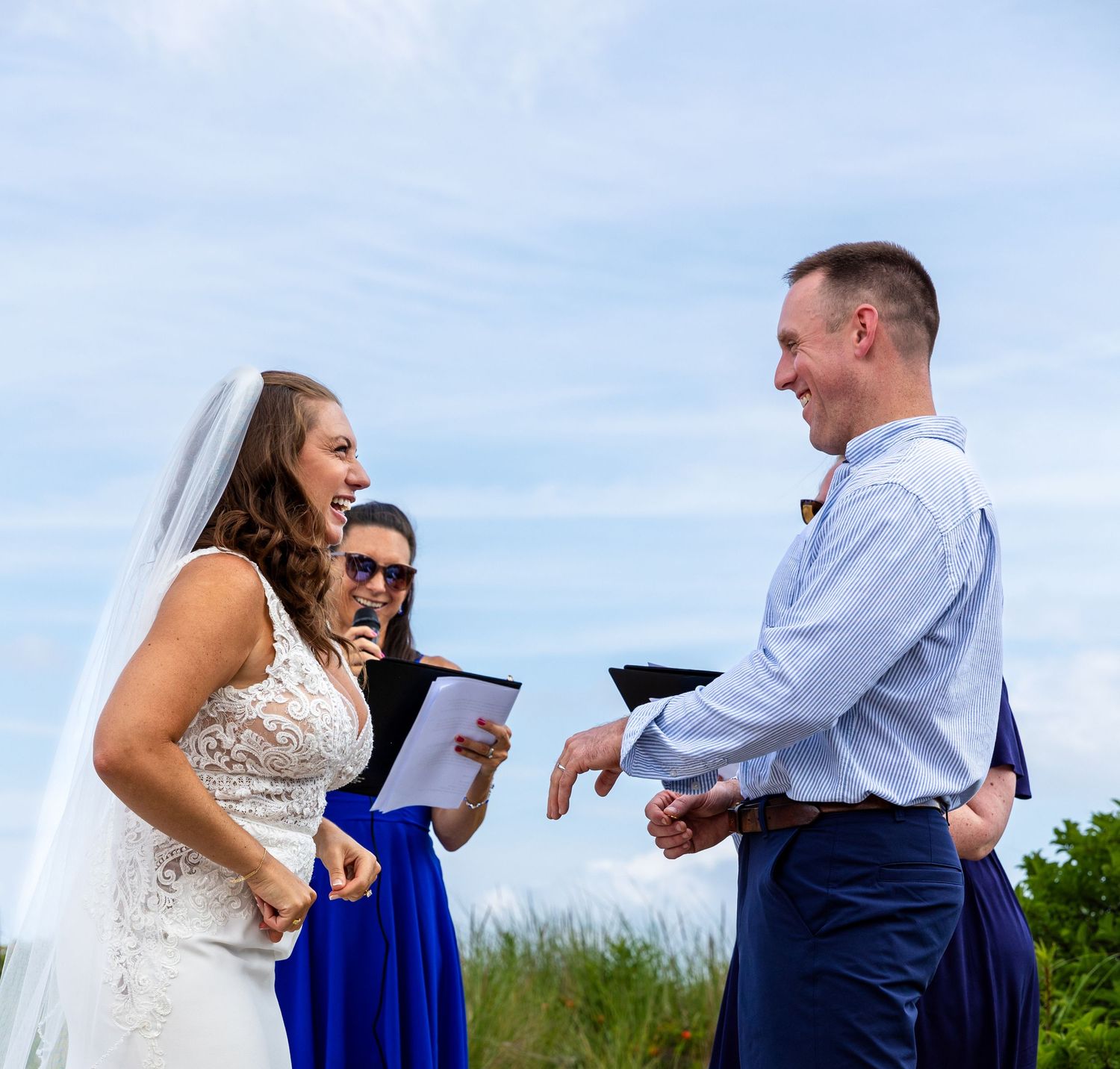A couple in wedding attire stand in an outdoor field looking at a blue tablet or book together.