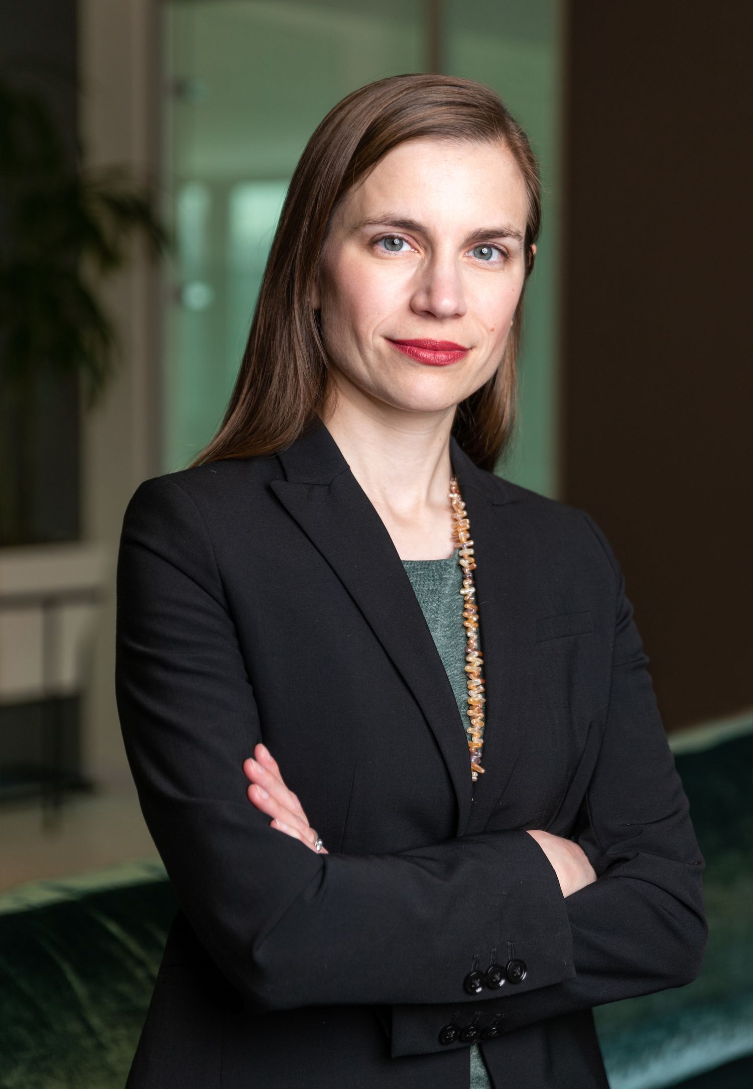 Professional in black blazer and green top stands confidently with arms crossed.