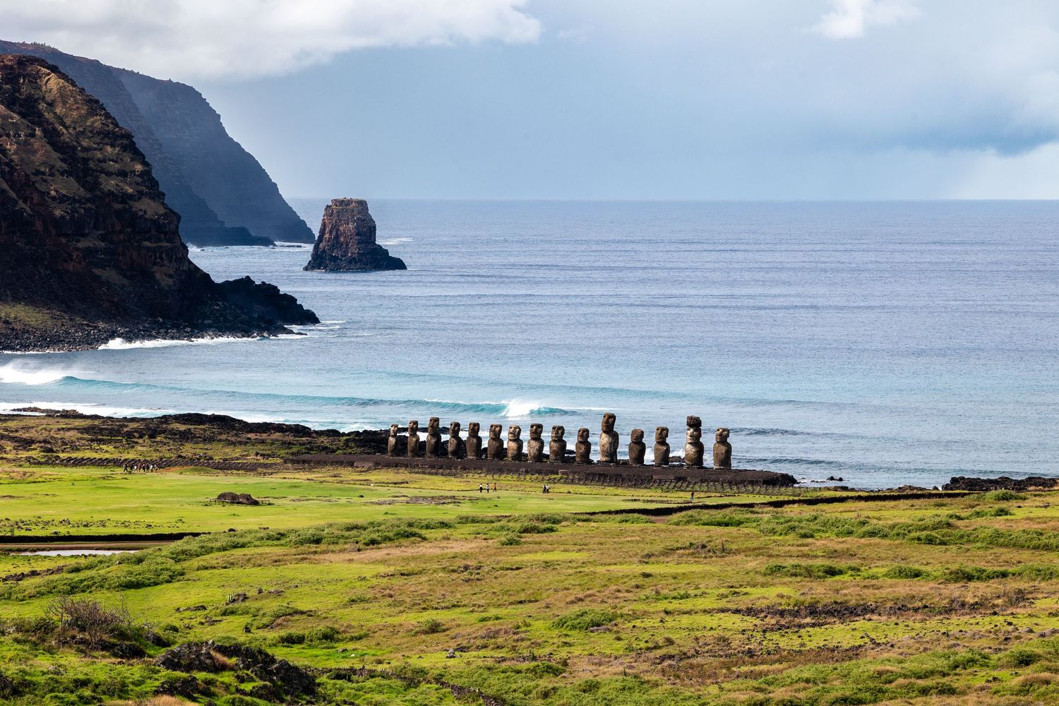 Row of ancient moai statues overlooking the ocean on Easter Island with rugged cliffs and green coastline.
