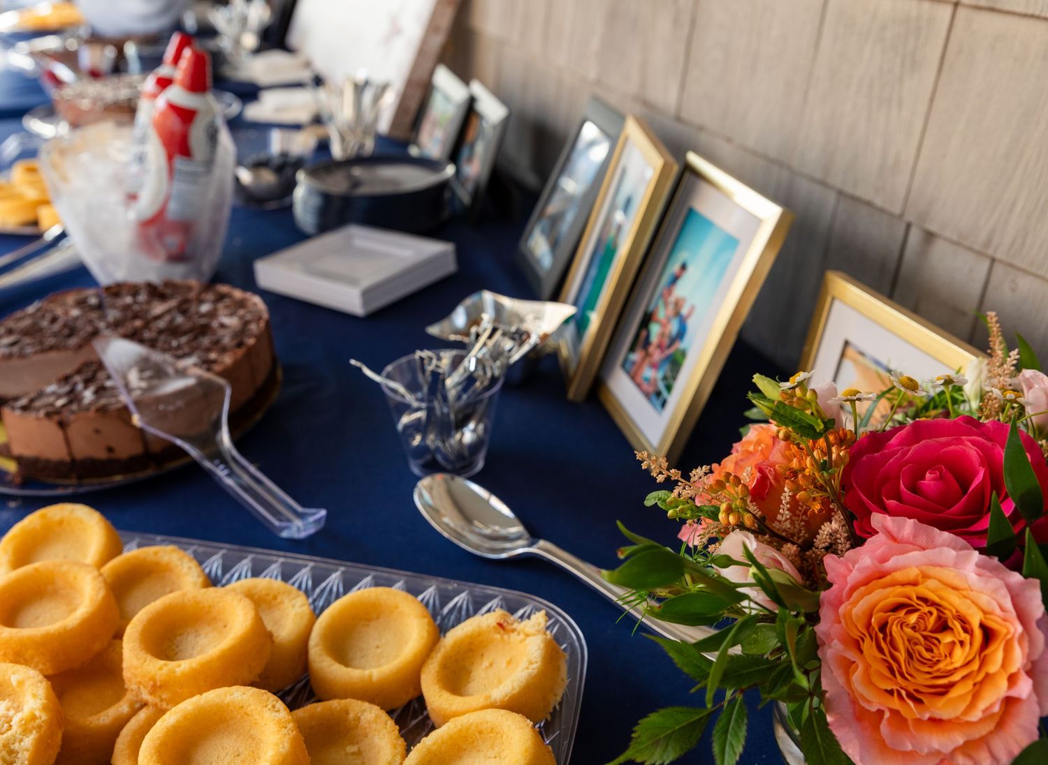 Appetizing display of rustic pastries, colorful flowers, and elegant table settings adorned with orange roses at a catered event.