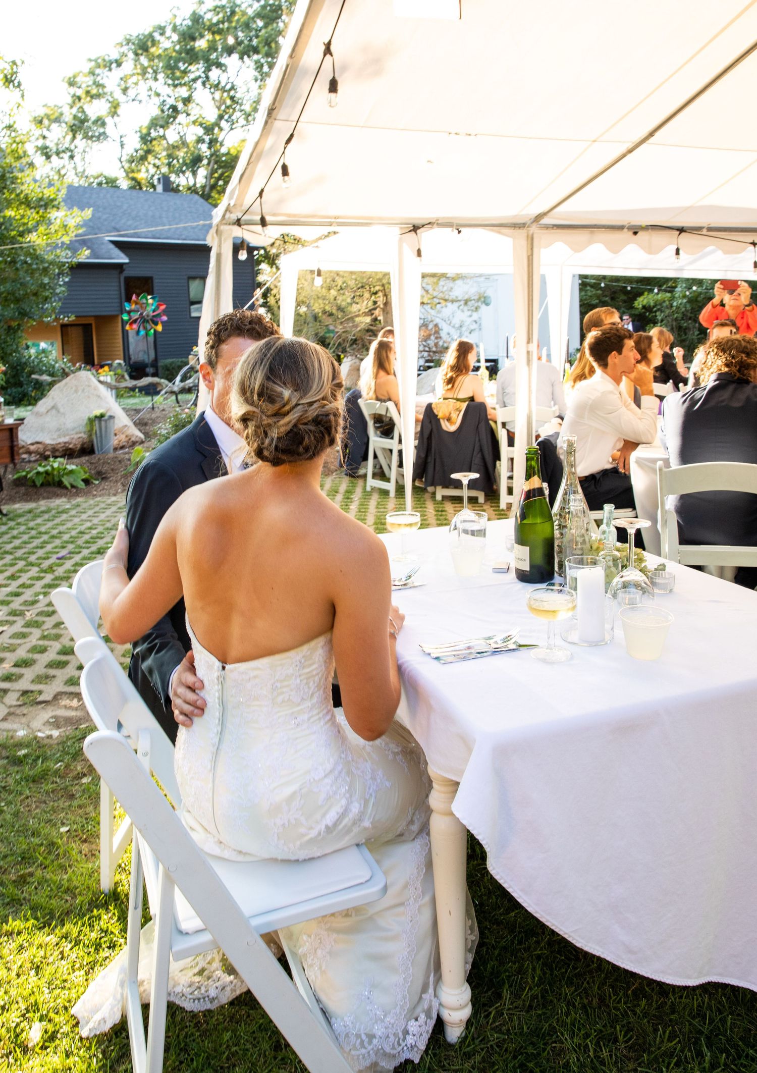Reception guests dine under an elegant white tent at a backyard wedding venue during golden hour.