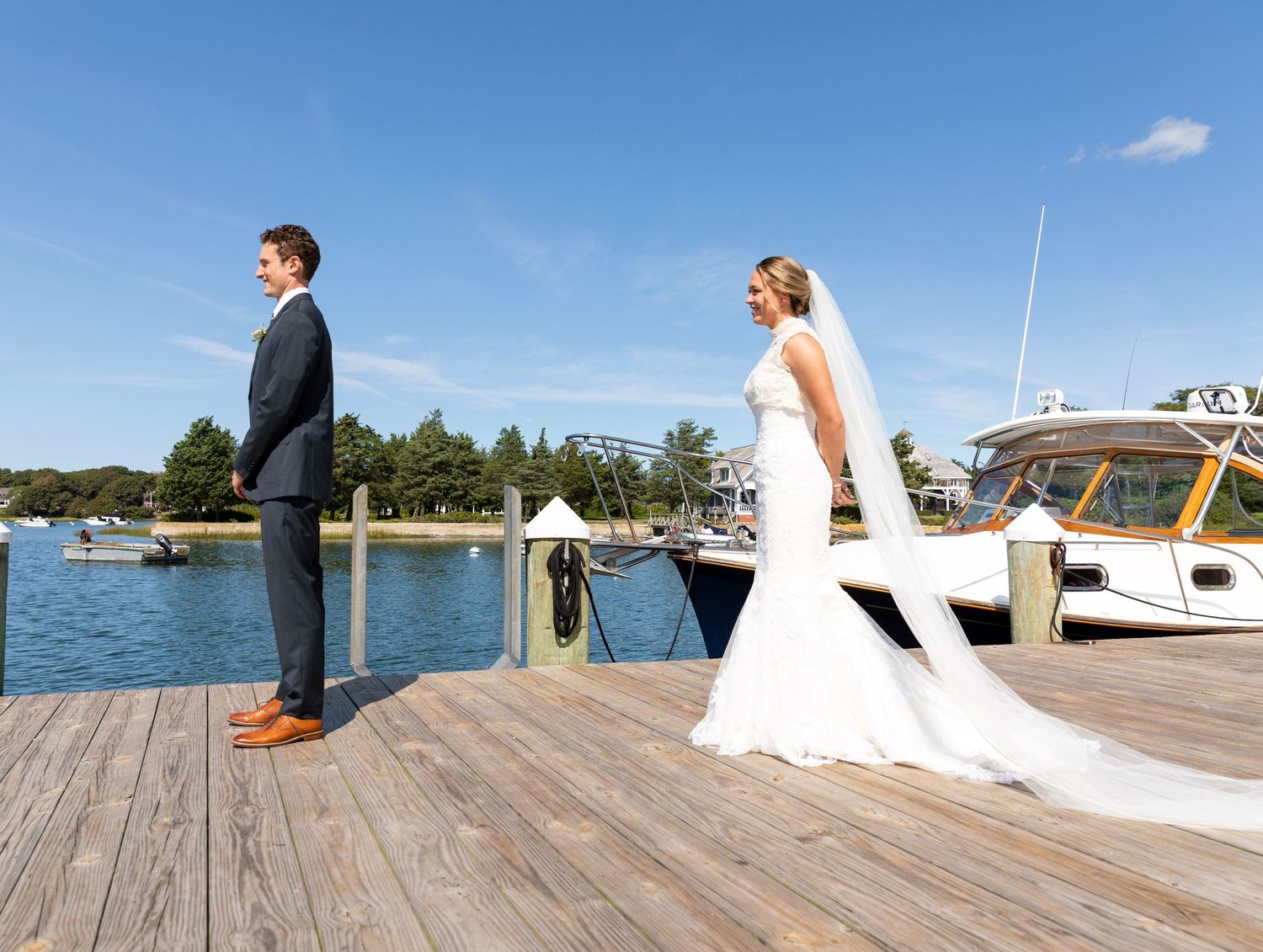 Wedding couple sits on rustic wooden dock overlooking marina and waterfront on their special day.