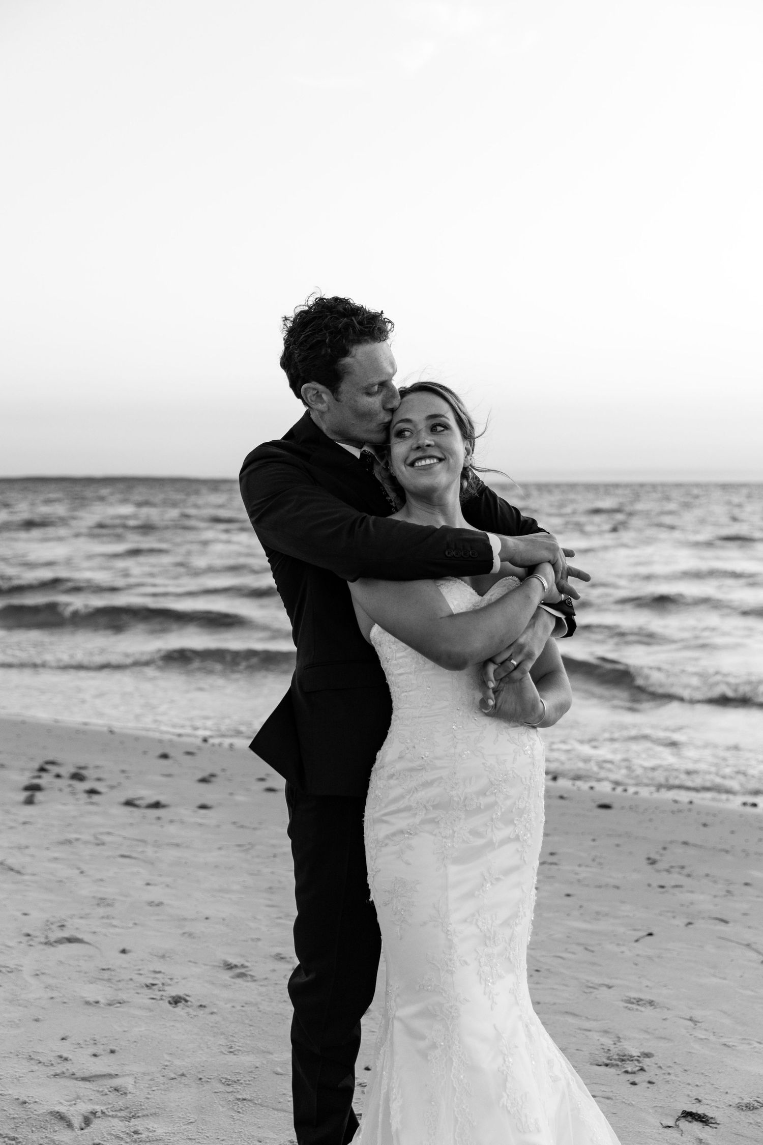 A black and white series of photos showing a couple embracing on a beach beside the ocean.