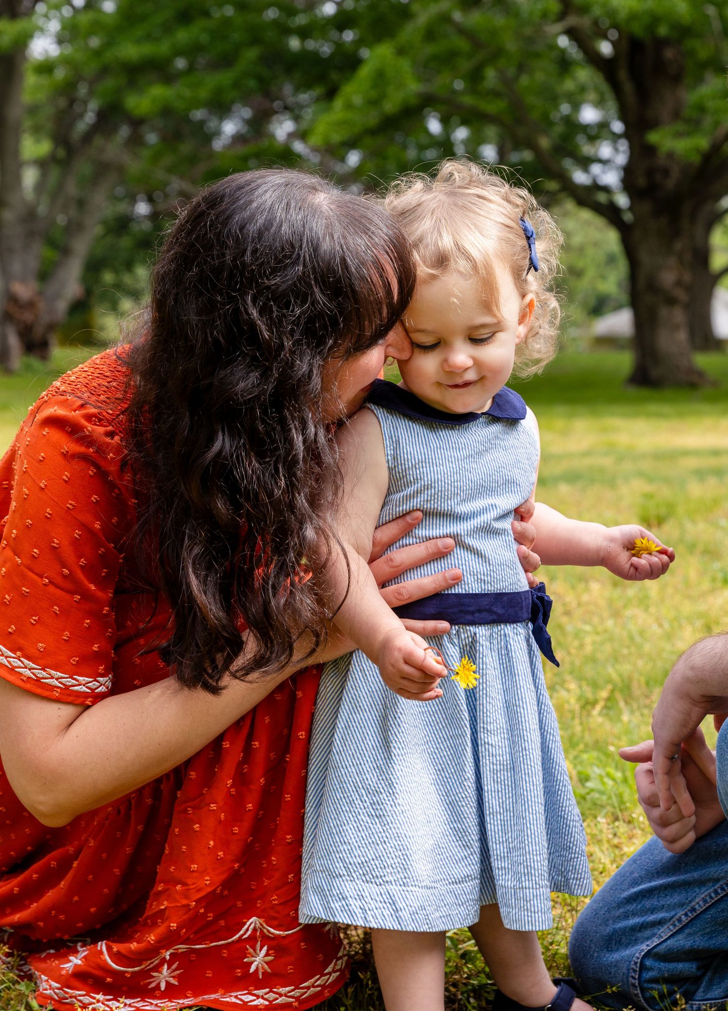A caregiver in an orange lace dress playing and engaging with a small child outdoors in a lush park setting.
