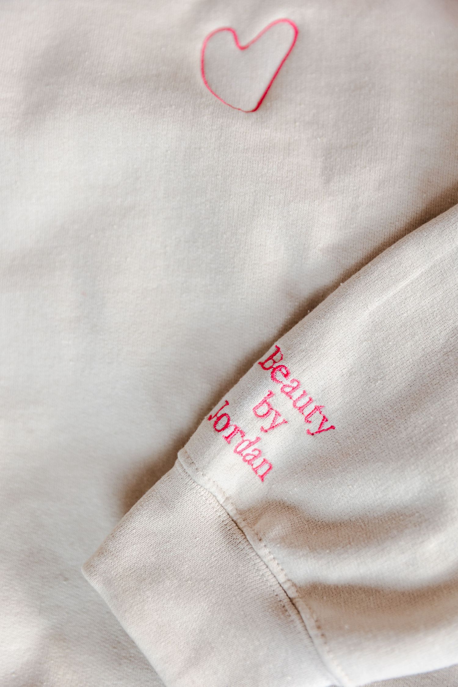 A white garment with pink embroidered text and a small heart design drawn in pink.