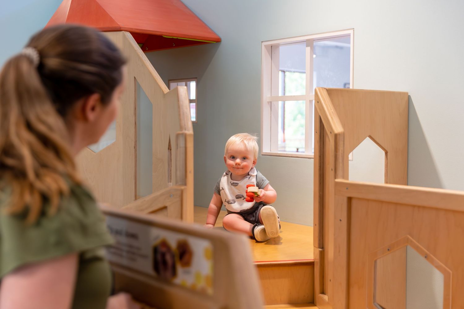 A sequence of images showing a wooden dollhouse being played with in a sunlit indoor space.