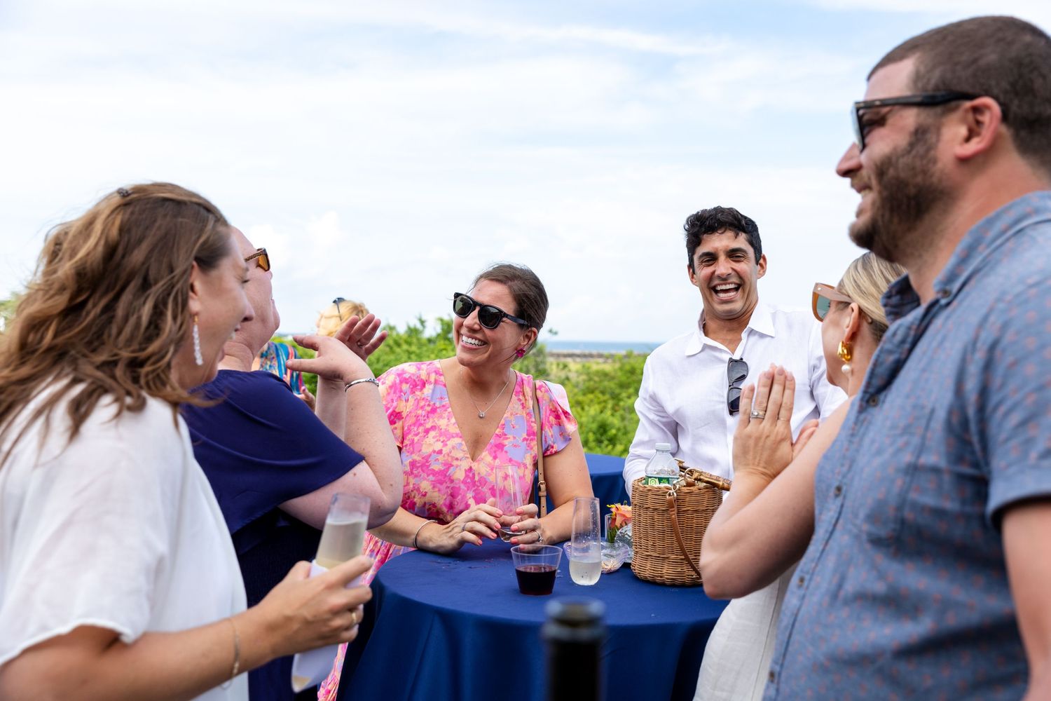 Group of friends laughing and socializing at outdoor party with drinks.