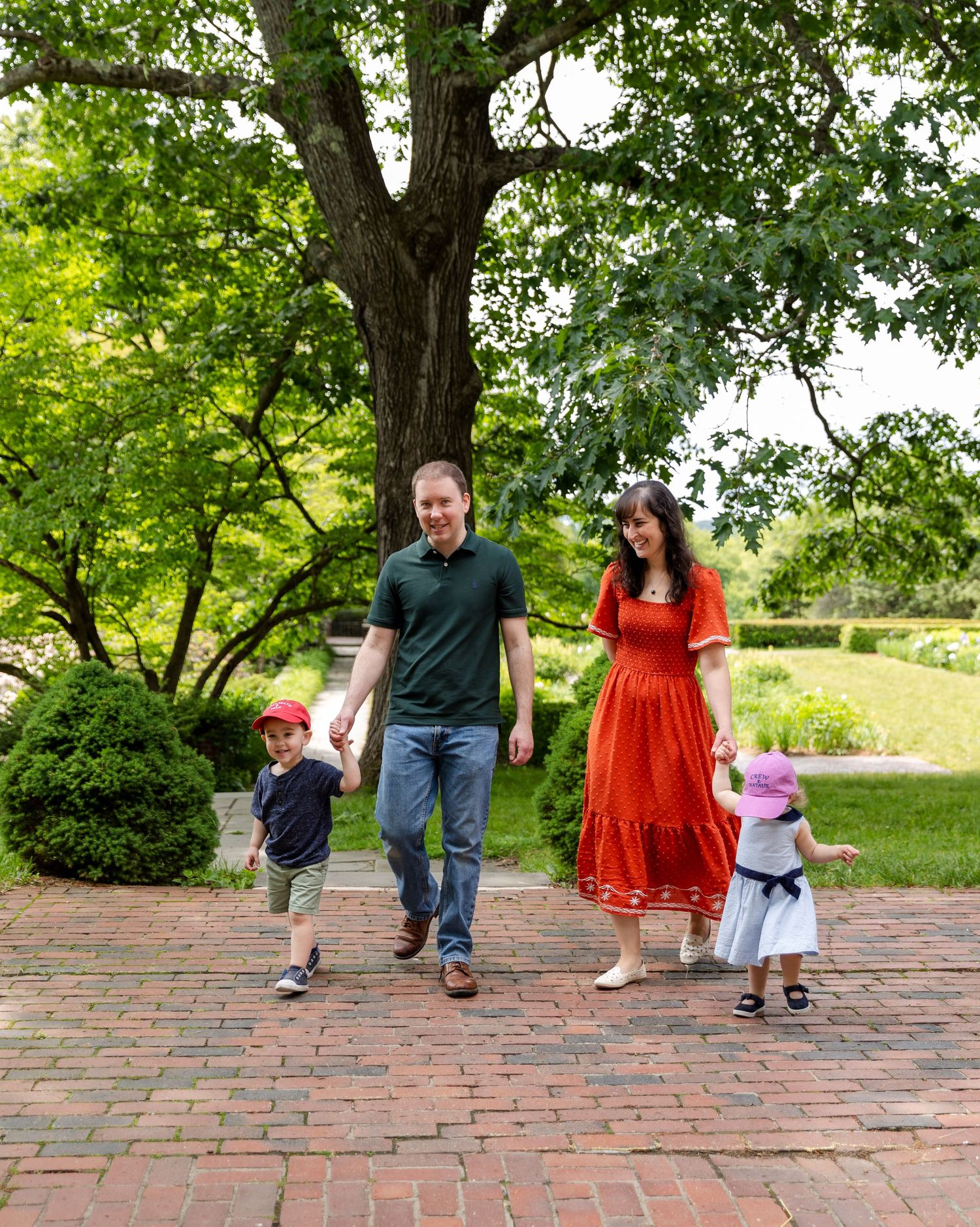 A couple and their child moving together across red brick pavement in a lush garden setting.