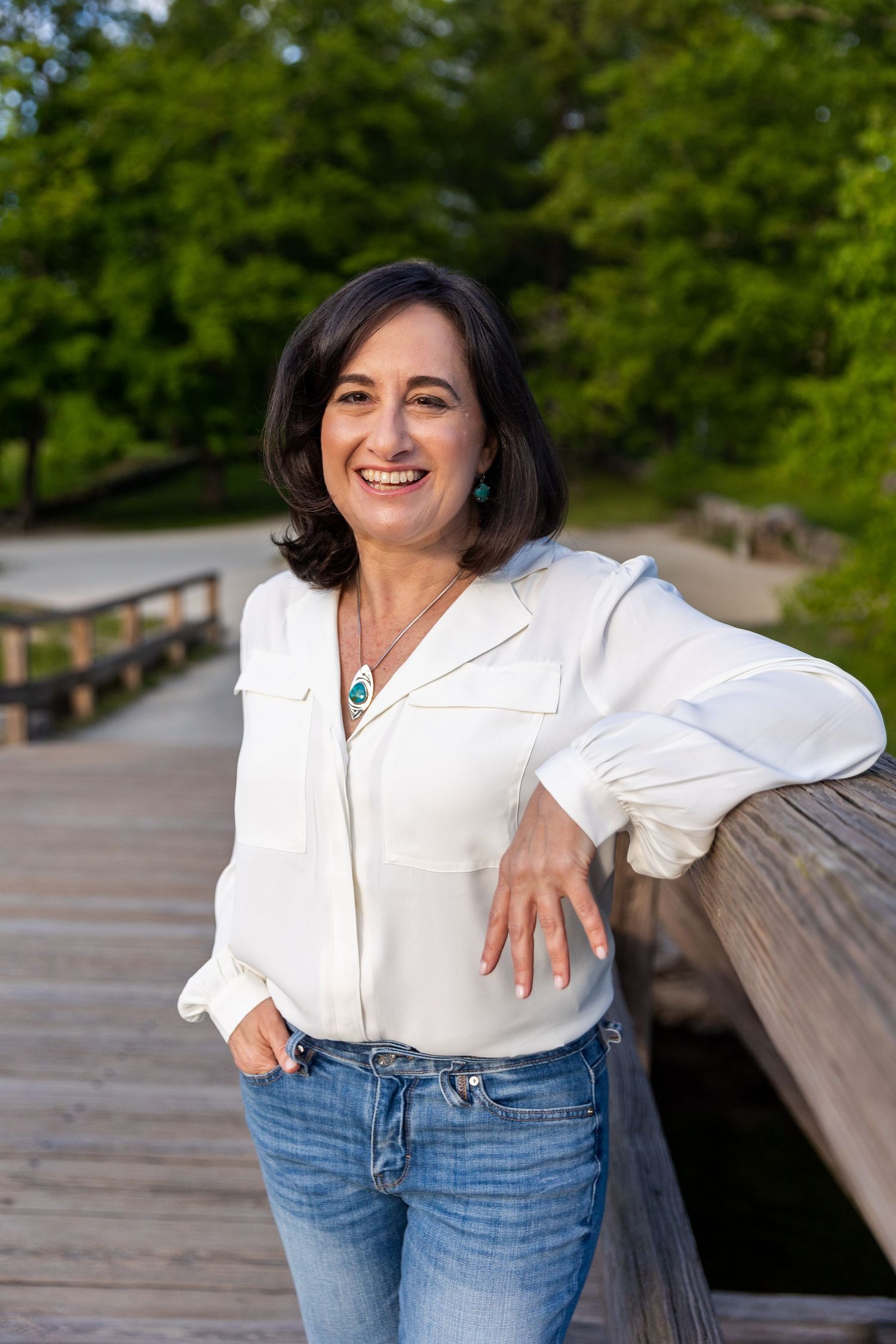 Woman in white button-down shirt leans casually against wooden railing outdoors.
