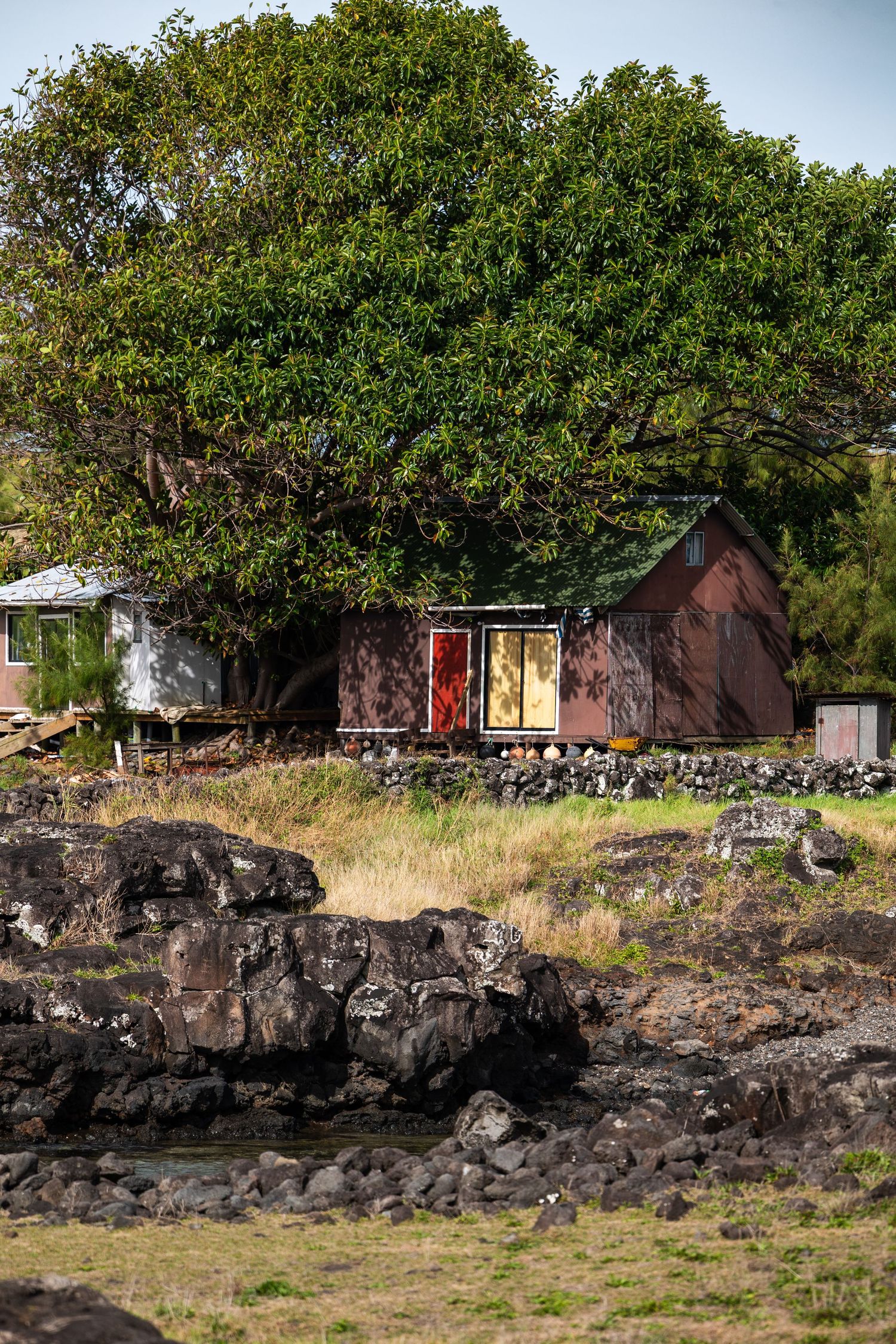 Red and brown cabins nestled along rocky volcanic coastline with lush green trees in Hawaii.