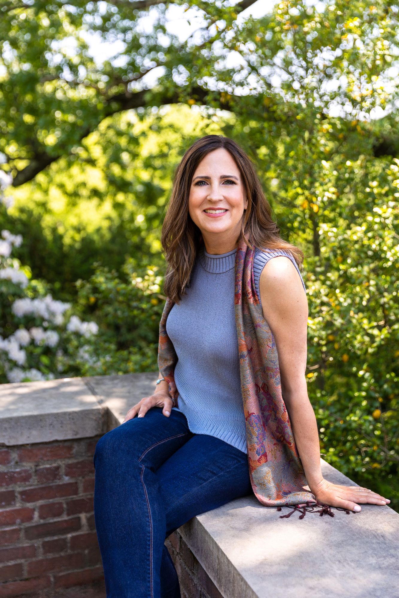 Outdoor portrait on brick wall wearing blue sweater and patterned scarf.