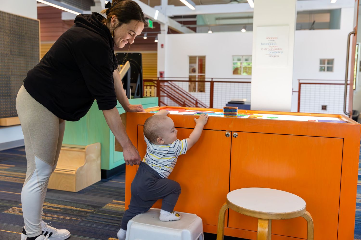 People work at bright orange desks in a modern coworking space with white walls and natural lighting.