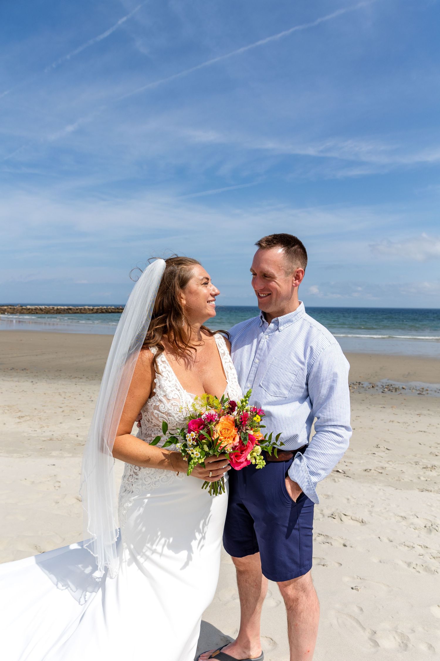 A couple shares a joyful moment on a sunny beach with white sand and blue ocean waters in the background.