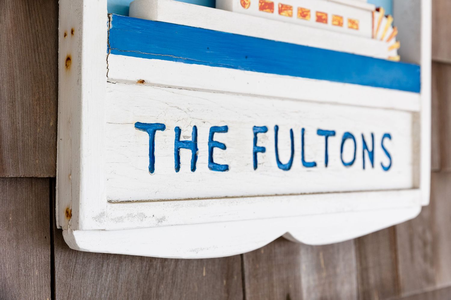 Wooden mailboxes labeled 'THE FULTONS' mounted on a rustic gray fence in a row.