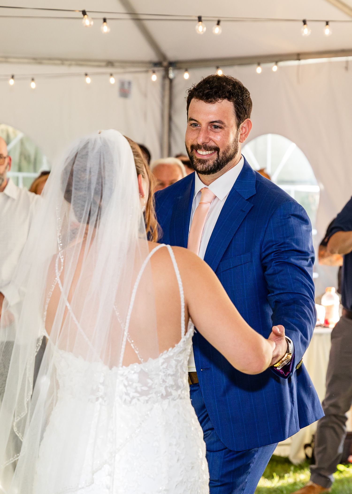 Newlyweds share intimate moments during their first dance in a white tent reception space with twinkling lights.