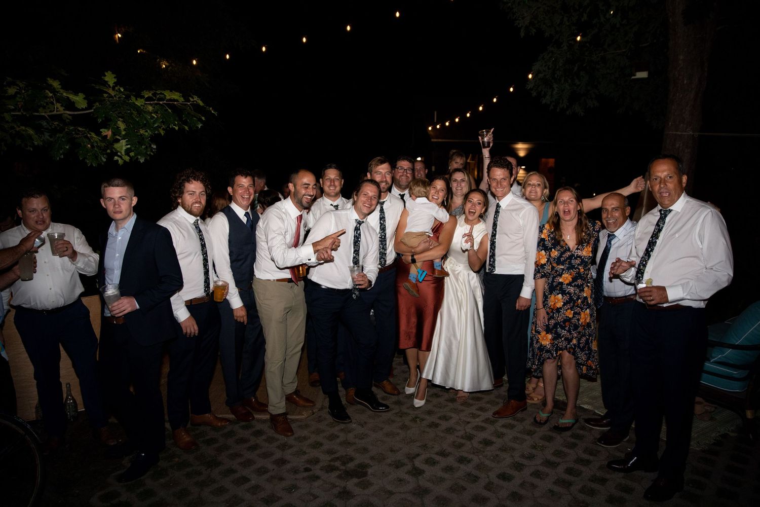 Wedding guests gathered on a patio under string lights for a fun evening dance celebration at an outdoor reception.