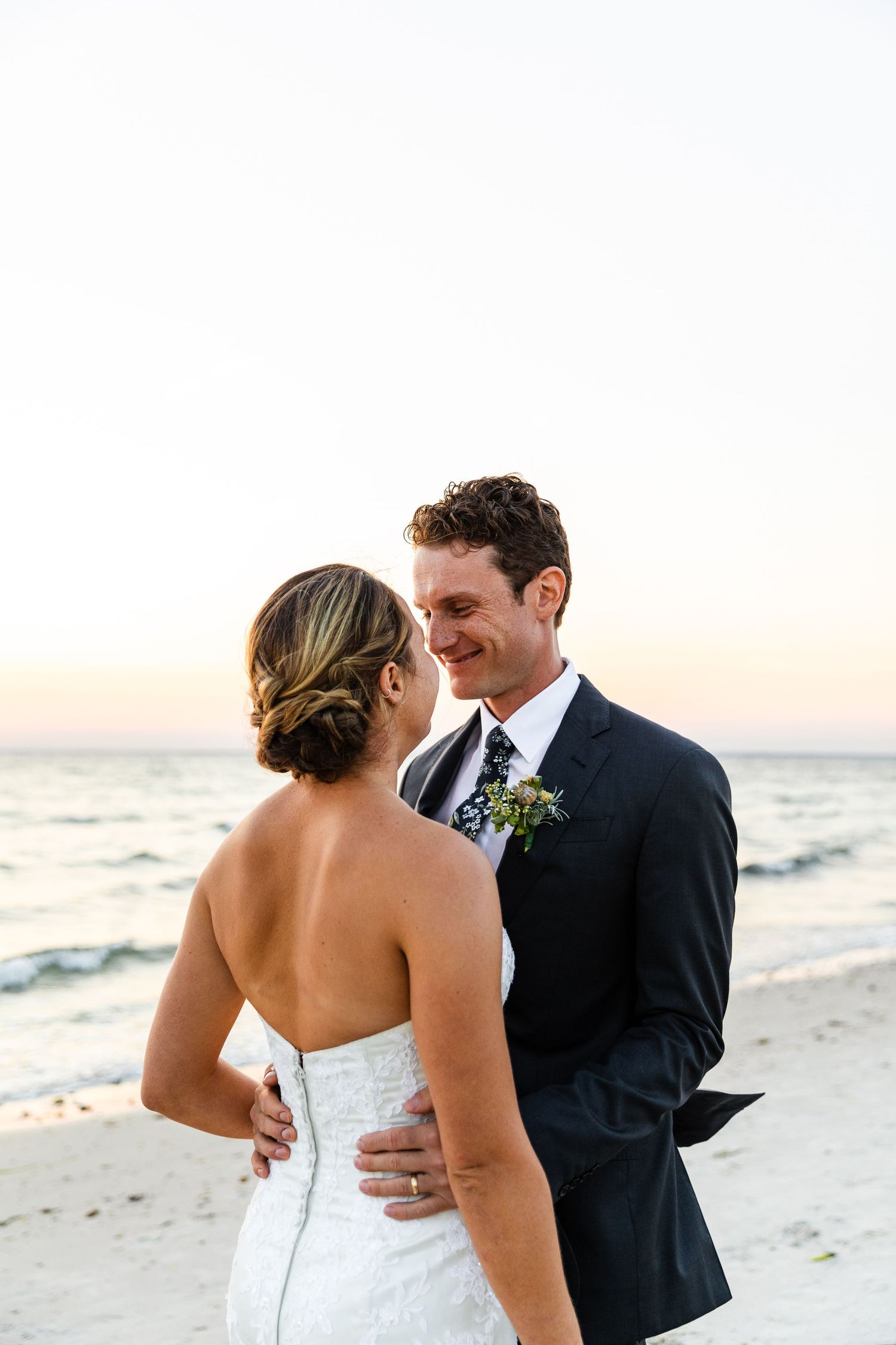 A couple shares an intimate moment on a sandy beach during sunset at their oceanfront wedding.