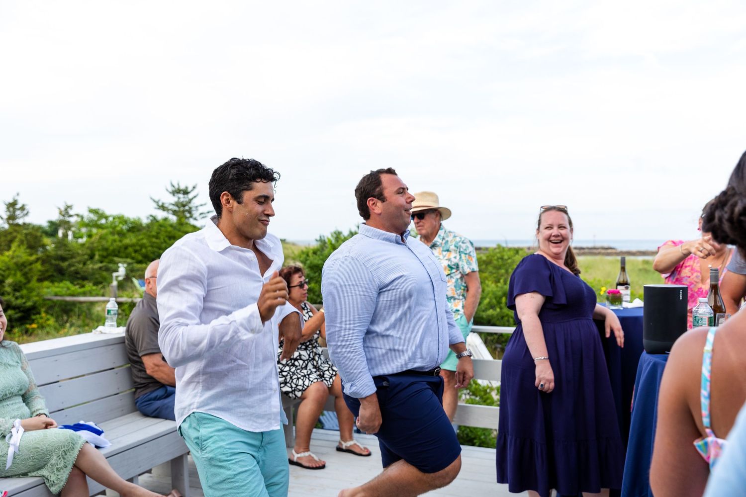 Groups of wedding guests engaged in casual conversation at an outdoor reception venue with water views.